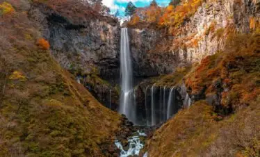 Tall Nikko waterfall cascading down rocky cliffs surrounded by autumn colors.