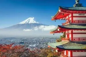 Snow-capped Mount Fuji viewed behind the red Chureito Pagoda surrounded by autumn leaves.